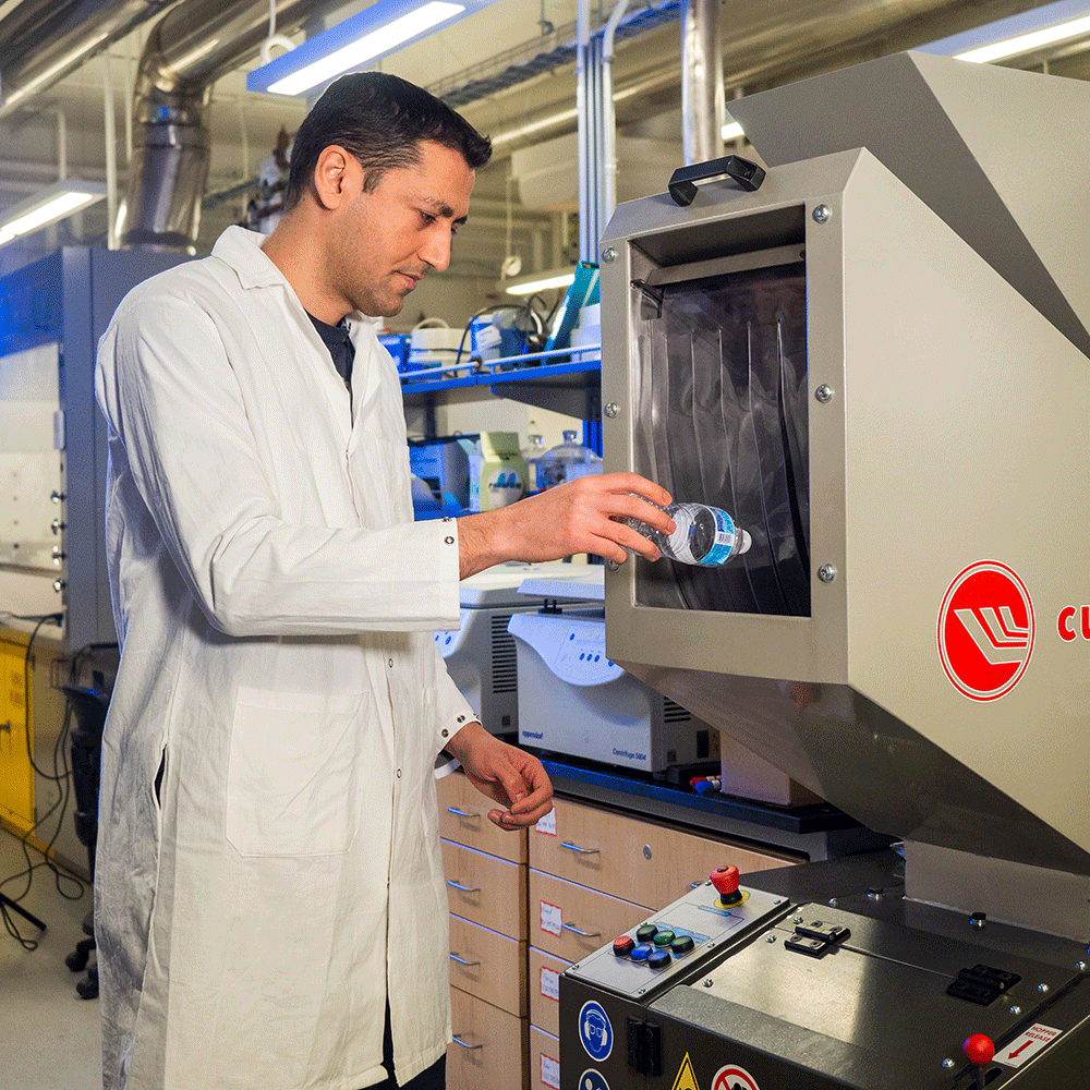 Dr. Mohammad Arjmand putting a used plastic water bottle into a machine.